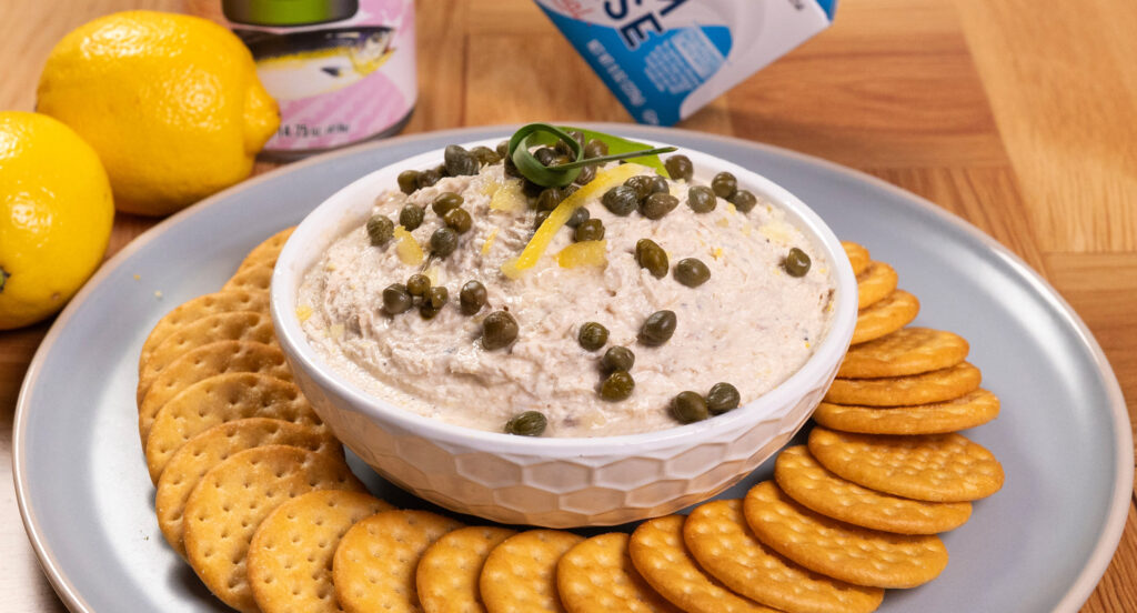 Dip cremoso de pescado decorado con alcaparras y limón, servido con galletitas saladas.